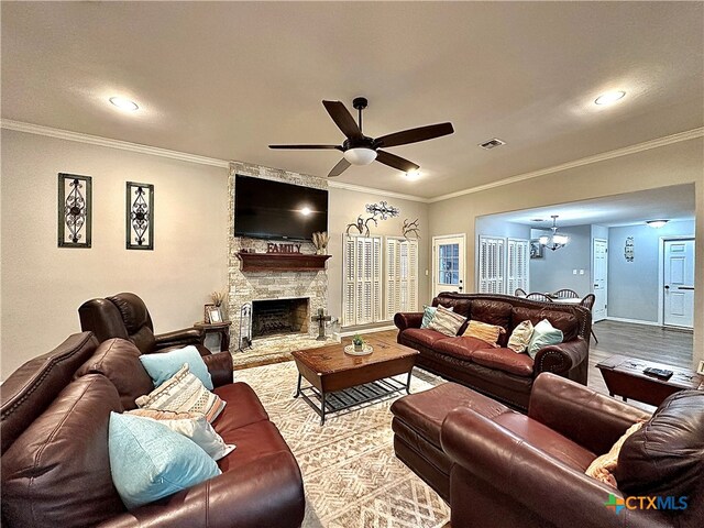 living room with a stone fireplace, ceiling fan with notable chandelier, wood-type flooring, and crown molding