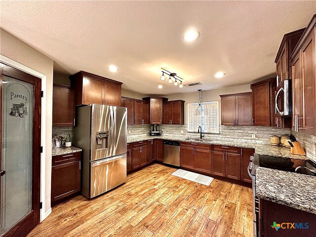 kitchen with stainless steel appliances, tasteful backsplash, light stone countertops, light wood-type flooring, and decorative light fixtures