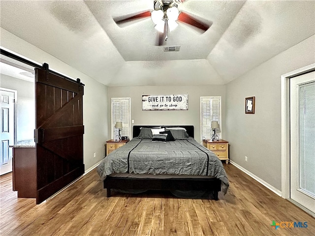 bedroom with a barn door, a textured ceiling, hardwood / wood-style floors, lofted ceiling, and ceiling fan