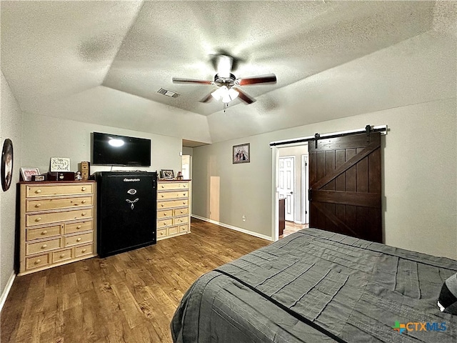 bedroom featuring a textured ceiling, a barn door, dark hardwood / wood-style floors, vaulted ceiling, and ceiling fan