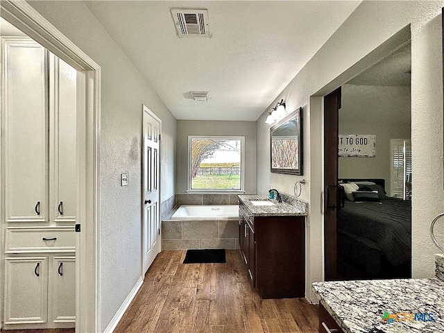 bathroom with hardwood / wood-style floors, vanity, and tiled tub