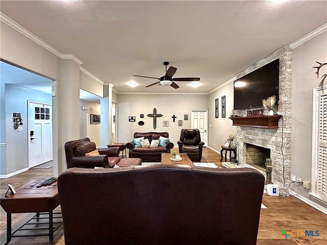 living room featuring a stone fireplace, ceiling fan, hardwood / wood-style floors, and ornamental molding