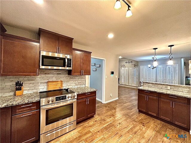 kitchen with light stone counters, appliances with stainless steel finishes, decorative light fixtures, a chandelier, and light hardwood / wood-style flooring