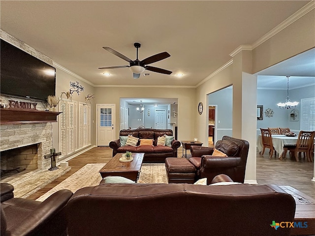 living room with wood-type flooring, ceiling fan with notable chandelier, a stone fireplace, and crown molding