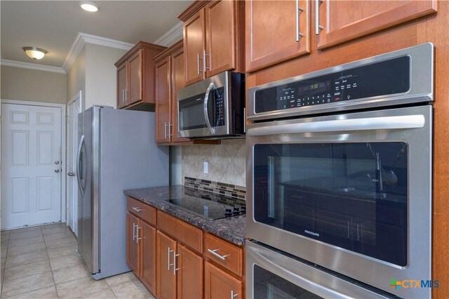 kitchen featuring light tile patterned flooring, crown molding, dark stone countertops, stainless steel appliances, and decorative backsplash