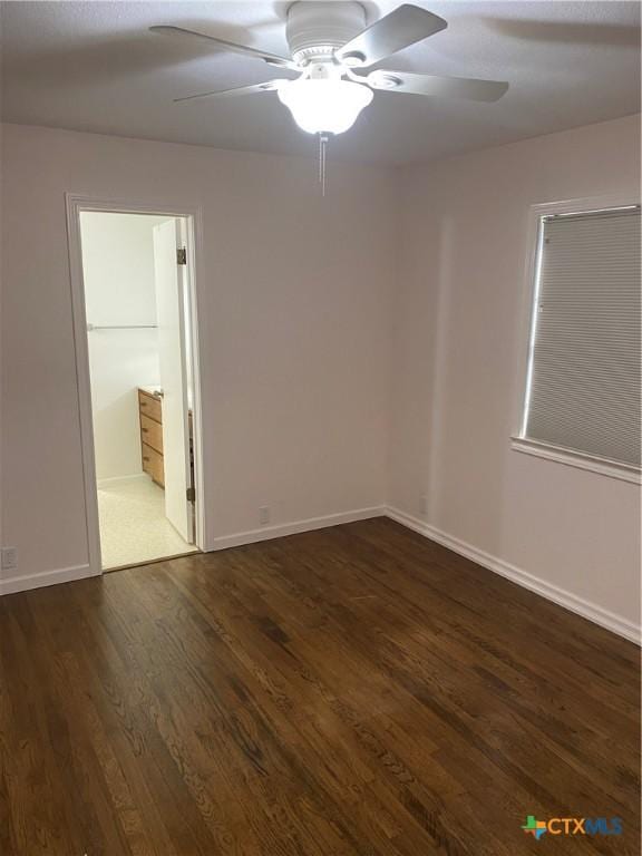 empty room with ceiling fan, dark wood finished floors, and baseboards