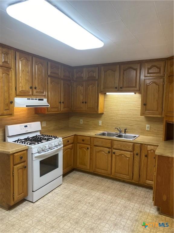 kitchen featuring white gas stove, a sink, light countertops, range hood, and light floors