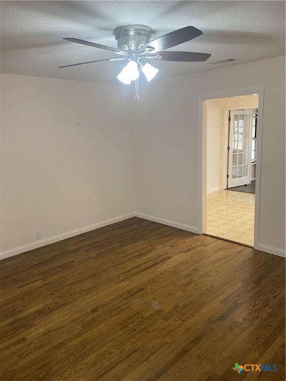 unfurnished room with visible vents, baseboards, ceiling fan, and dark wood-type flooring