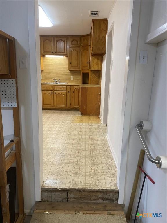 kitchen with light floors, tasteful backsplash, visible vents, brown cabinetry, and a sink