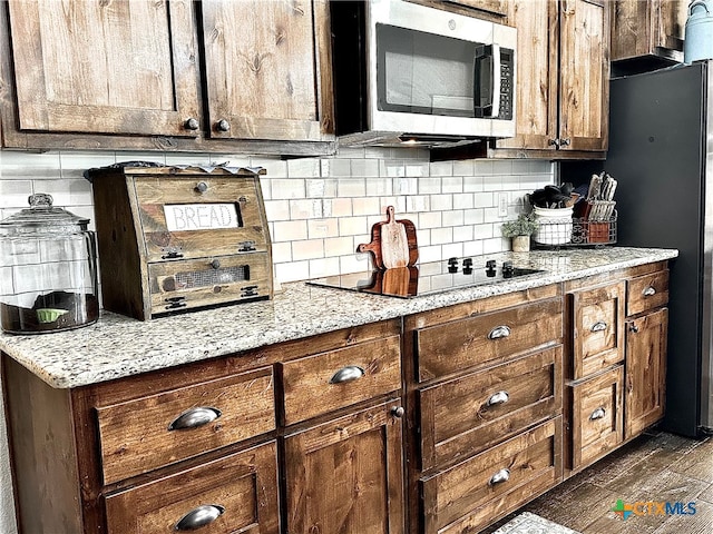 kitchen with decorative backsplash, dark hardwood / wood-style flooring, black appliances, and light stone counters