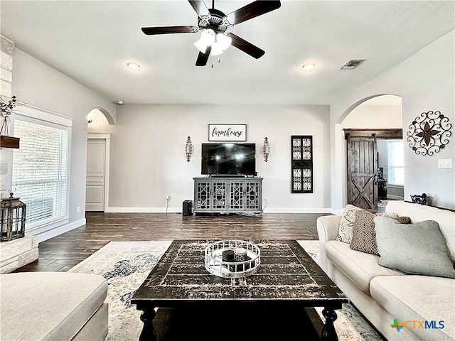 living room featuring dark wood-type flooring, a barn door, and ceiling fan