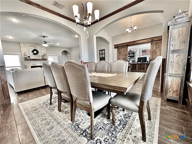 dining room with dark hardwood / wood-style flooring, a stone fireplace, and ceiling fan with notable chandelier