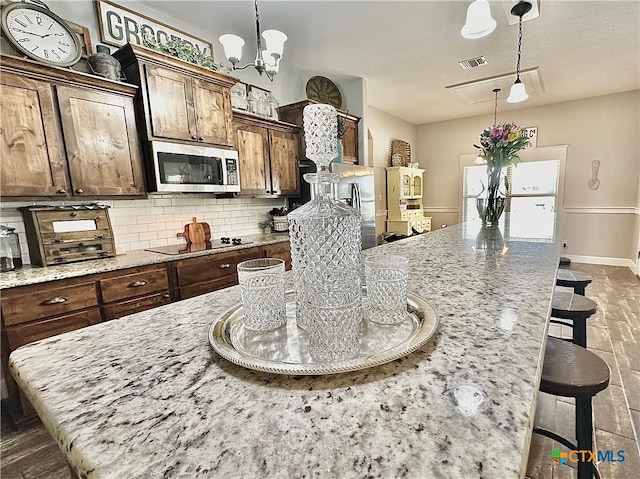 kitchen with black electric stovetop, decorative light fixtures, light stone countertops, a breakfast bar, and a center island