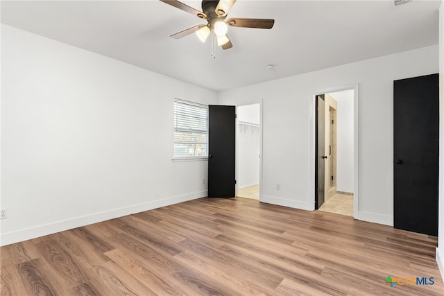 unfurnished bedroom featuring ceiling fan, a spacious closet, a closet, and light wood-type flooring