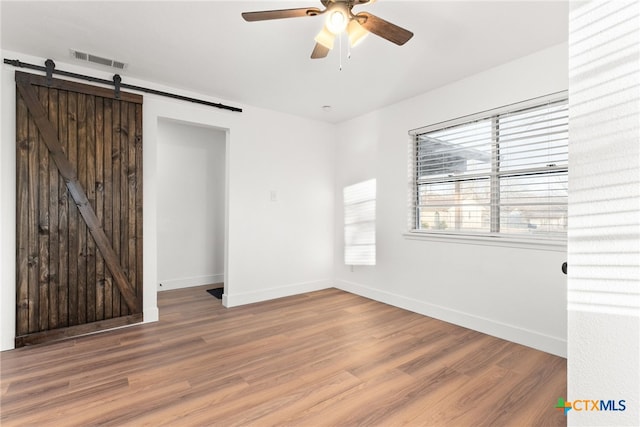 empty room featuring hardwood / wood-style floors, ceiling fan, and a barn door