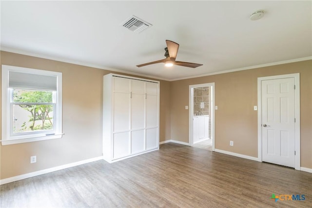 unfurnished bedroom featuring wood finished floors, visible vents, ornamental molding, a closet, and baseboards