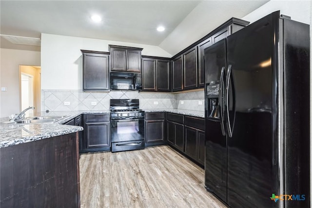 kitchen featuring light wood finished floors, decorative backsplash, light stone countertops, black appliances, and a sink