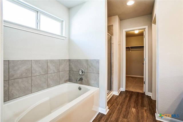 full bath featuring a garden tub, wood finished floors, baseboards, a shower stall, and a walk in closet