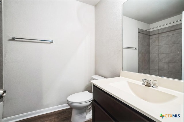 bathroom with toilet, wood finished floors, vanity, baseboards, and a shower