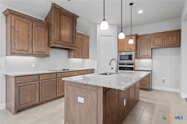 kitchen with stainless steel appliances, backsplash, light stone countertops, sink, and an island with sink