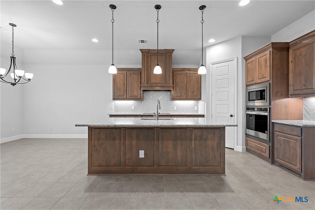 kitchen featuring appliances with stainless steel finishes, decorative light fixtures, light stone counters, and a kitchen island with sink