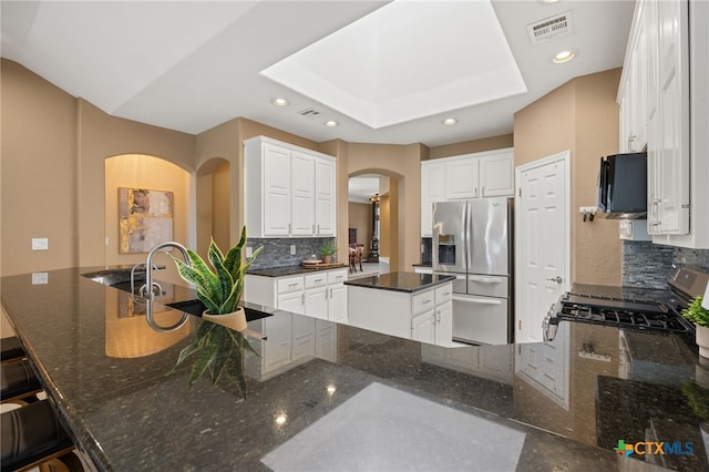 kitchen with a breakfast bar area, white cabinetry, dark stone countertops, stainless steel appliances, and kitchen peninsula