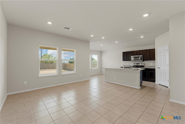 kitchen with light tile patterned flooring, appliances with stainless steel finishes, dark brown cabinets, sink, and an island with sink