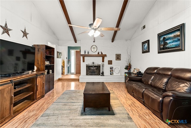 living area featuring visible vents, light wood-style flooring, a fireplace, ceiling fan, and vaulted ceiling with beams