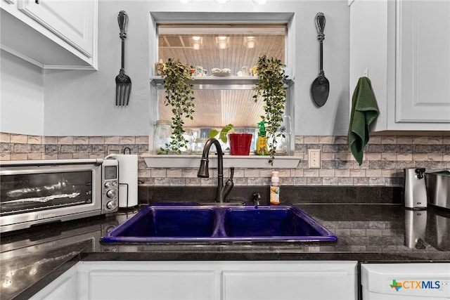 kitchen featuring a sink, backsplash, dark countertops, white cabinets, and a toaster