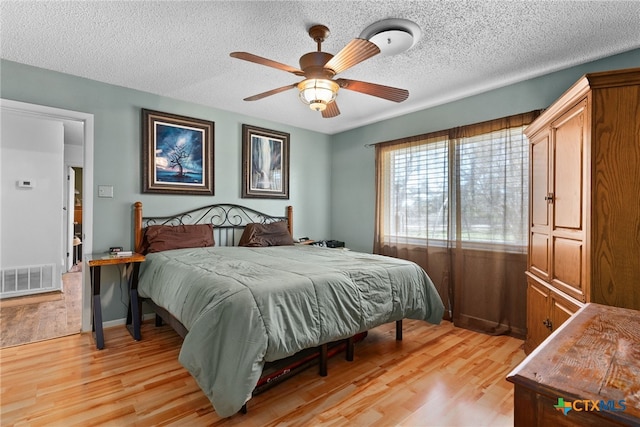 bedroom with light wood finished floors, visible vents, and a textured ceiling