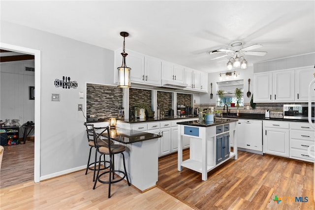 kitchen featuring white cabinetry, light wood-style flooring, dishwasher, dark countertops, and tasteful backsplash