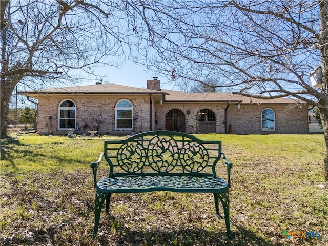 view of front of house with a shingled roof, a front yard, brick siding, and a chimney