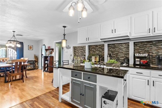 kitchen featuring dark countertops, white cabinets, light wood-type flooring, and under cabinet range hood