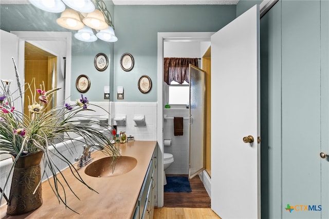 full bath featuring toilet, a stall shower, wood finished floors, tile walls, and vanity