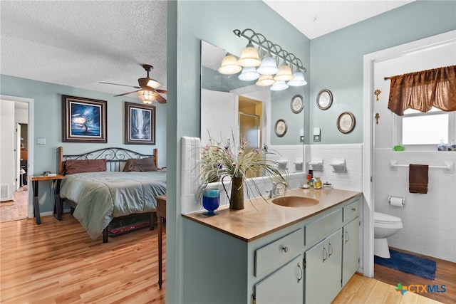 full bath with tile walls, toilet, wood finished floors, a textured ceiling, and a ceiling fan