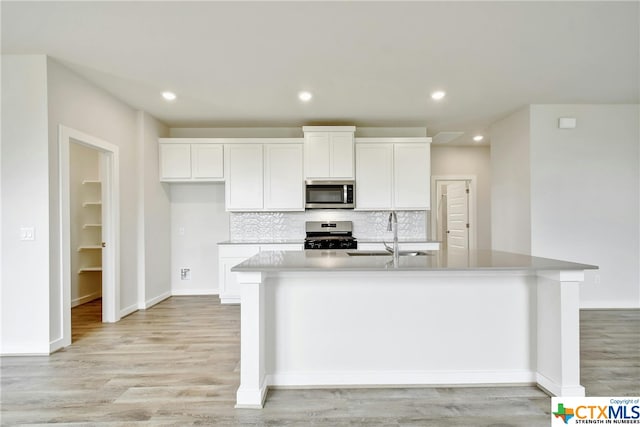 kitchen featuring appliances with stainless steel finishes, sink, an island with sink, light hardwood / wood-style floors, and white cabinets