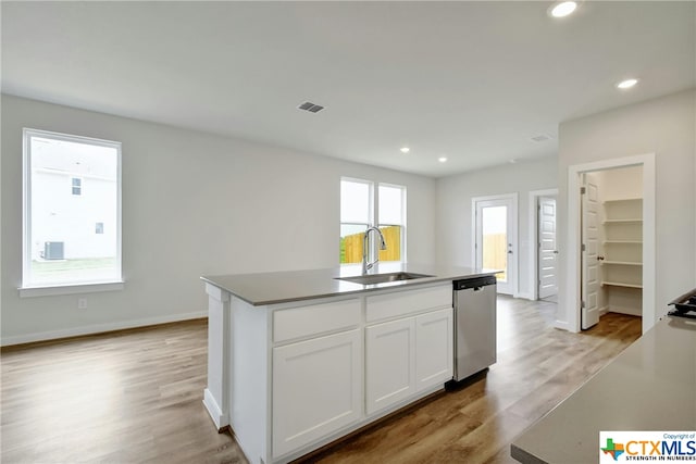 kitchen with a center island with sink, dishwasher, sink, white cabinetry, and light wood-type flooring