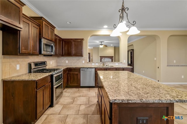 kitchen with sink, backsplash, hanging light fixtures, light stone counters, and stainless steel appliances