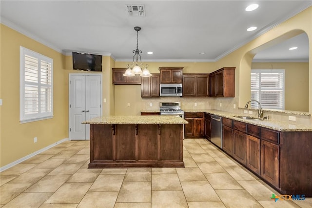 kitchen featuring sink, stainless steel appliances, ornamental molding, light stone countertops, and decorative light fixtures