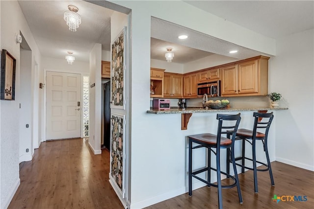 kitchen featuring stainless steel microwave, baseboards, a breakfast bar area, recessed lighting, and dark wood-style flooring