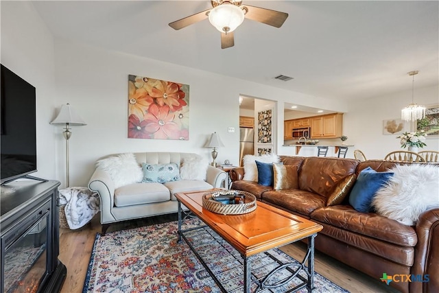 living area with visible vents, ceiling fan with notable chandelier, and light wood-type flooring