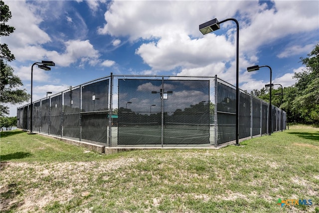 view of tennis court featuring a yard and fence