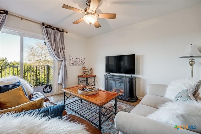 living room featuring a glass covered fireplace, baseboards, wood finished floors, and ceiling fan