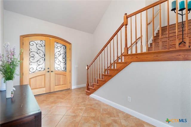 tiled entrance foyer with arched walkways, stairs, french doors, baseboards, and lofted ceiling