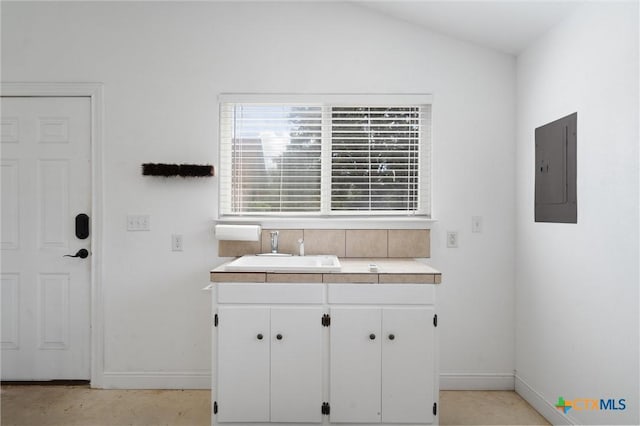 kitchen with electric panel, a sink, baseboards, white cabinets, and lofted ceiling