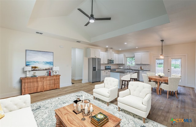 living room featuring a tray ceiling, lofted ceiling, ceiling fan, and light hardwood / wood-style flooring