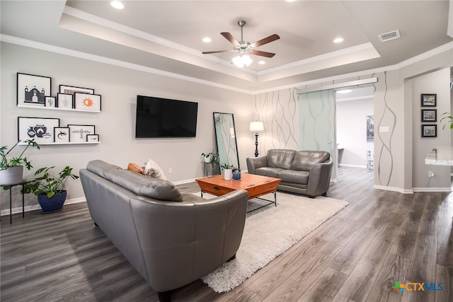 living room featuring a raised ceiling, ceiling fan, dark wood-type flooring, and ornamental molding