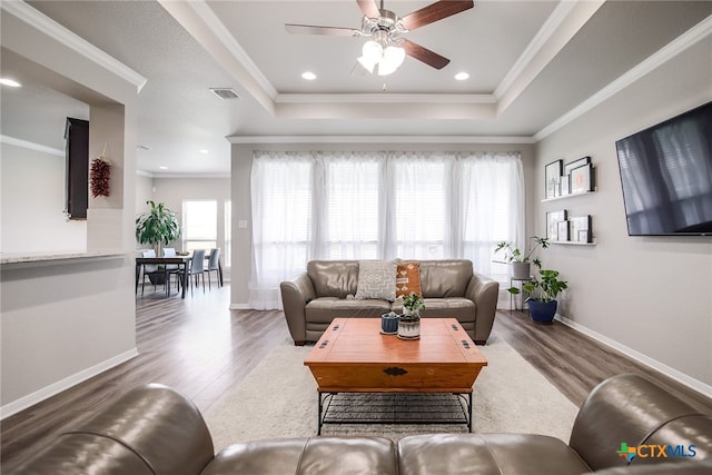 living room featuring hardwood / wood-style flooring, a tray ceiling, crown molding, and ceiling fan