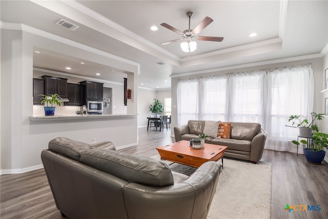 living room with a raised ceiling, sink, crown molding, ceiling fan, and dark hardwood / wood-style flooring