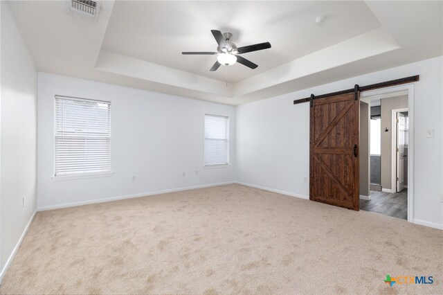 carpeted empty room featuring a barn door, a raised ceiling, and ceiling fan